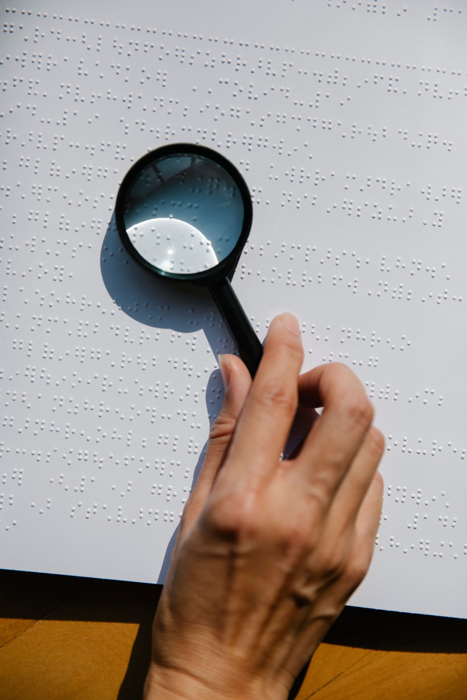 Hand holding a magnifying glass over a braille text page.