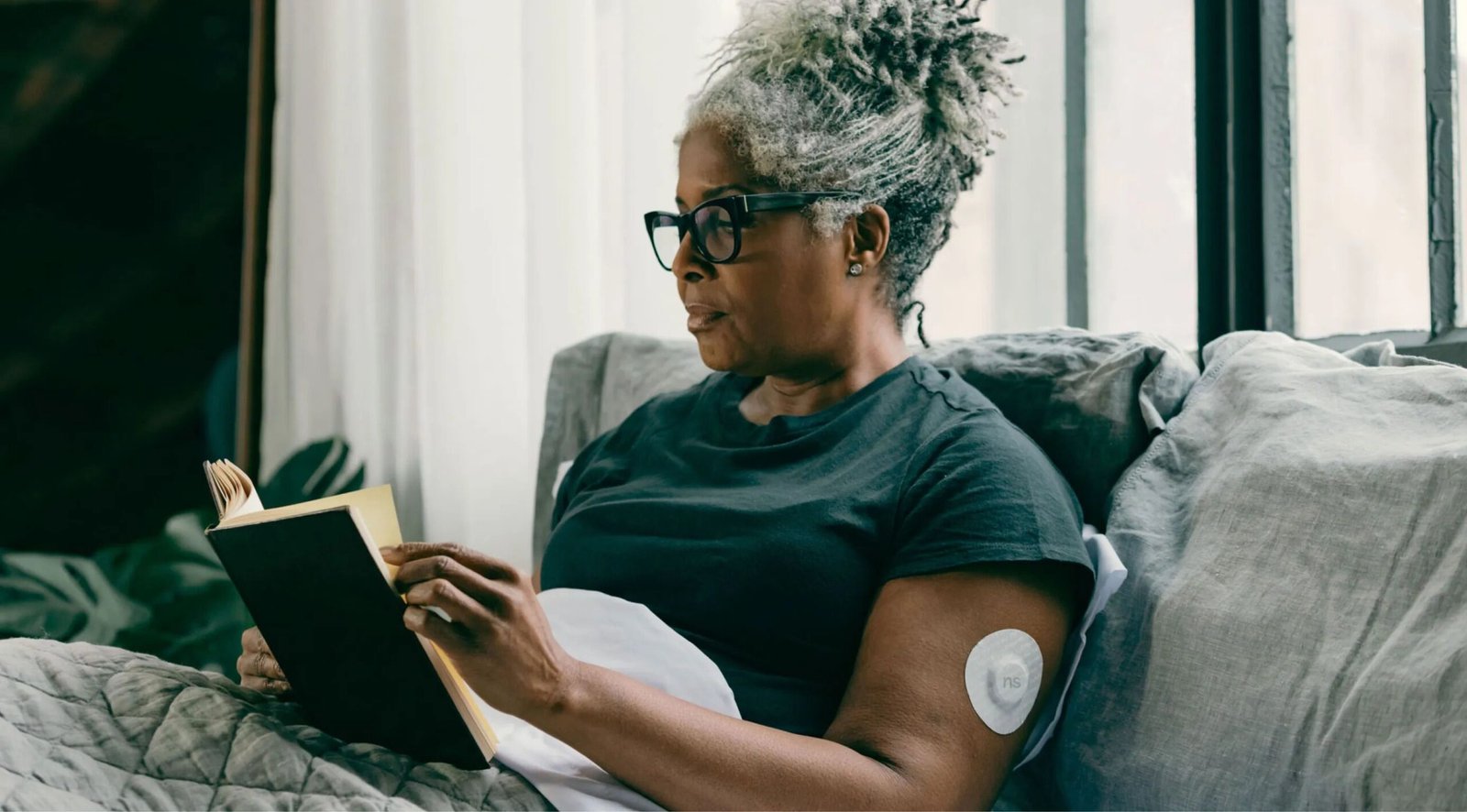 Older woman wearing a continuous glucose monitor while reading at home