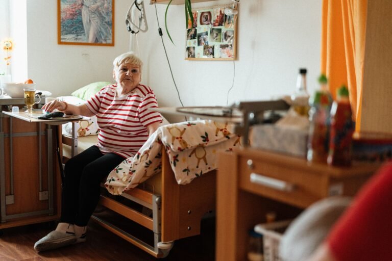 Older woman sitting on a bed in a retirement-home style room.