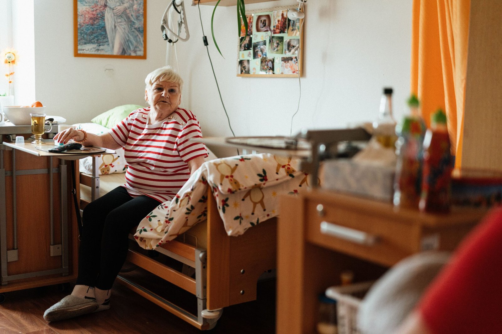 Older woman sitting on a bed in a retirement-home style room.