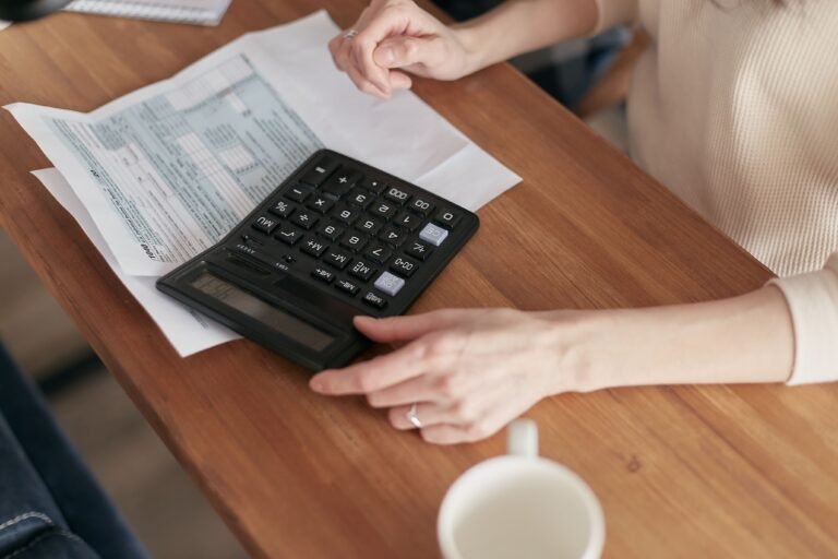 Person using a calculator to review a household budget at a desk.