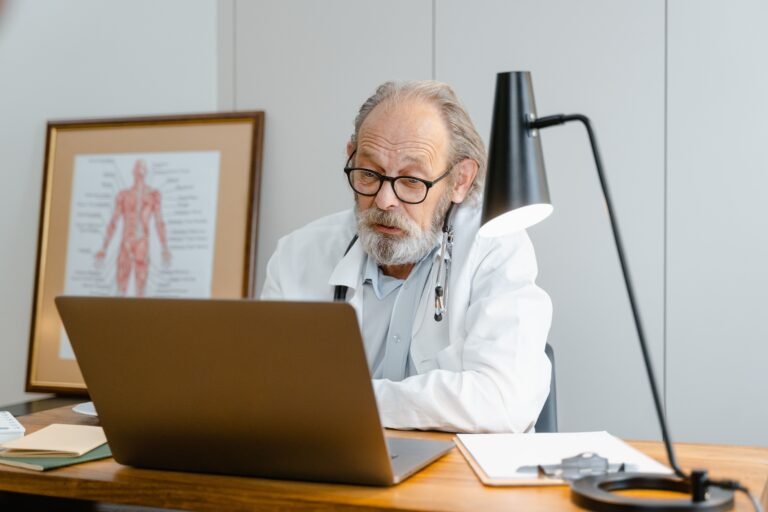 Older doctor using a laptop during a care-planning consultation.