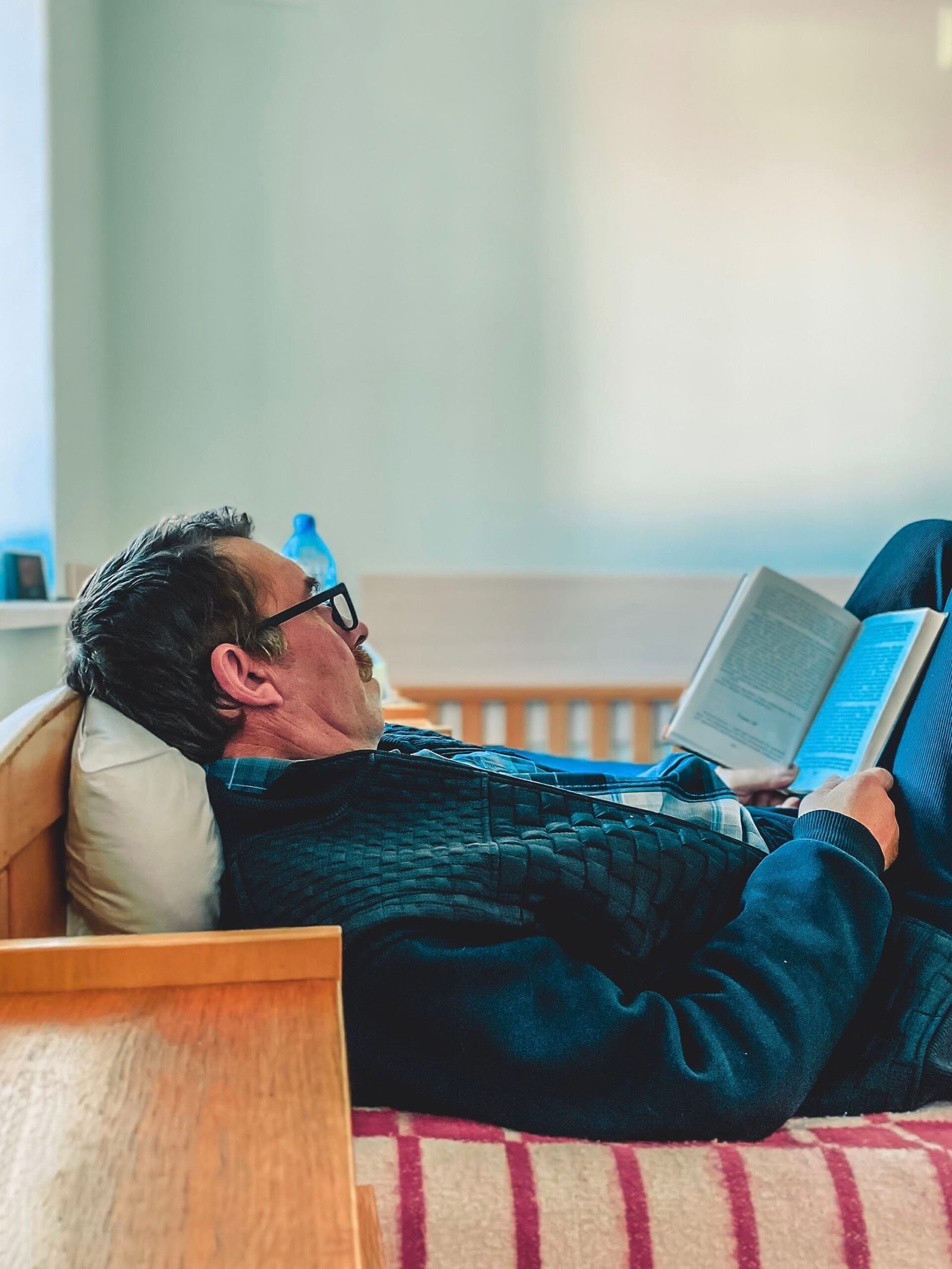 Older man reading a book while resting in bed