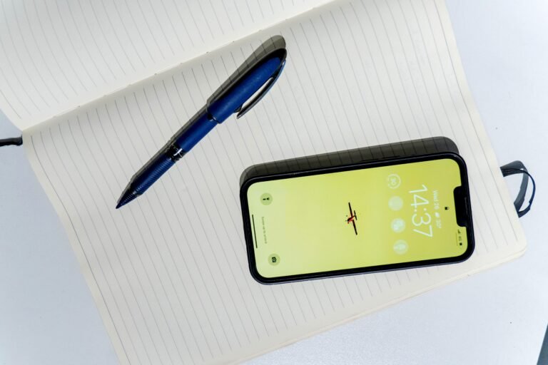 A smartphone and blue pen resting on an open lined notebook.