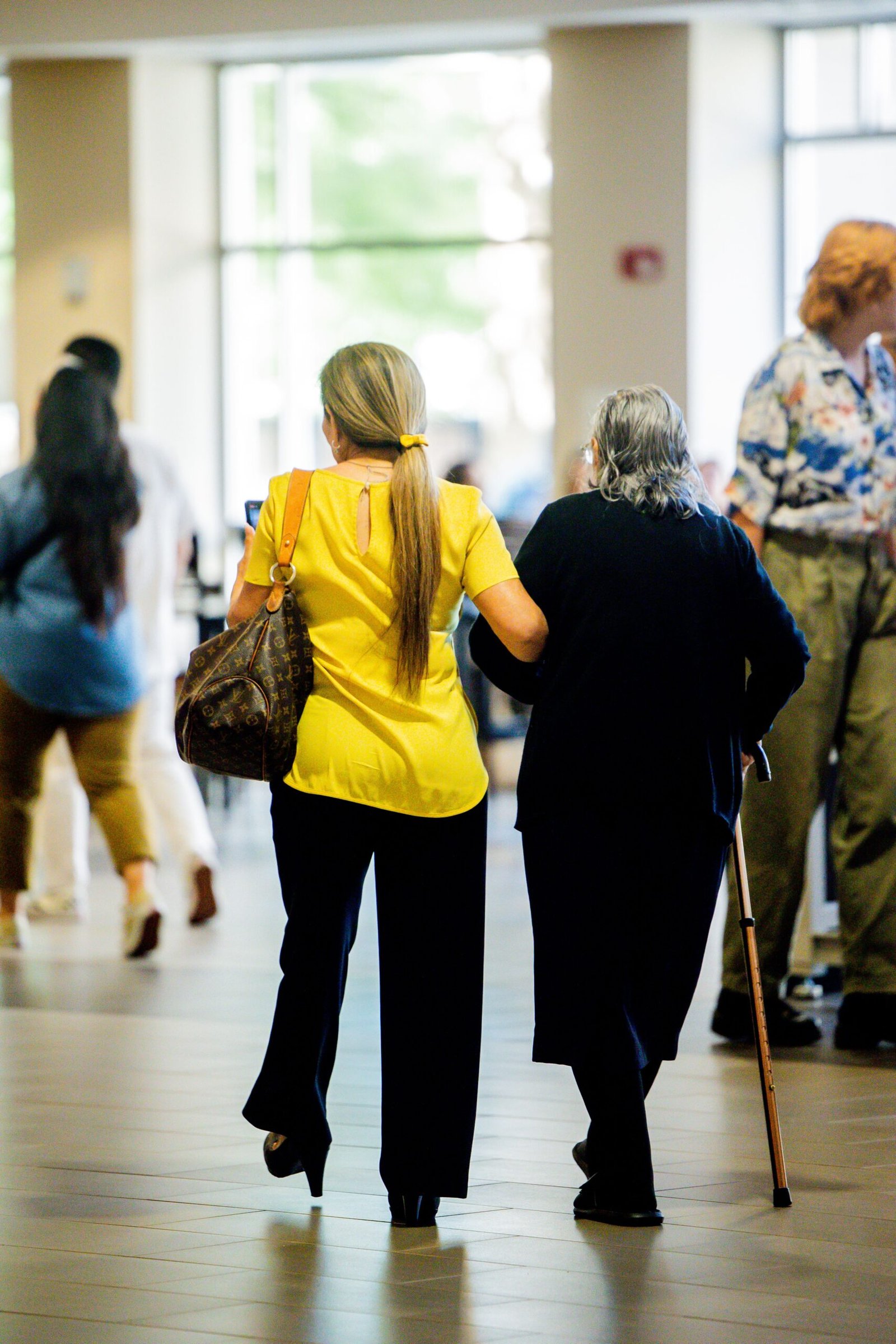 Caregiver supporting an older adult using a walking aid indoors.