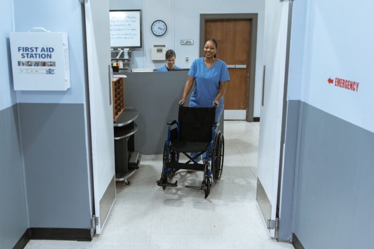Nurse pushing an empty wheelchair through a hospital hallway.