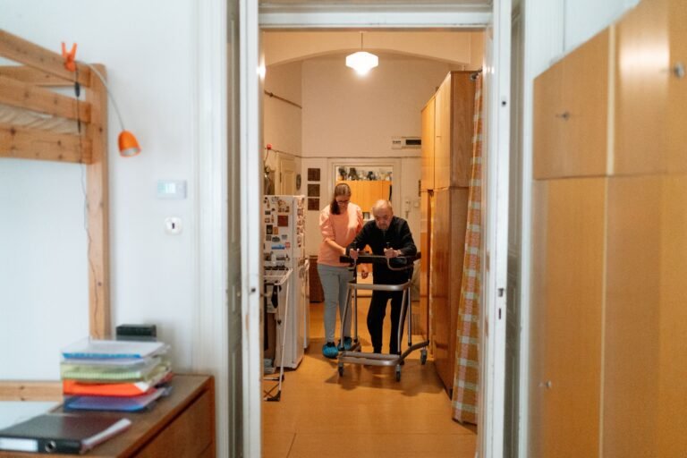 Caregiver supporting an older adult using a walker in a home setting.