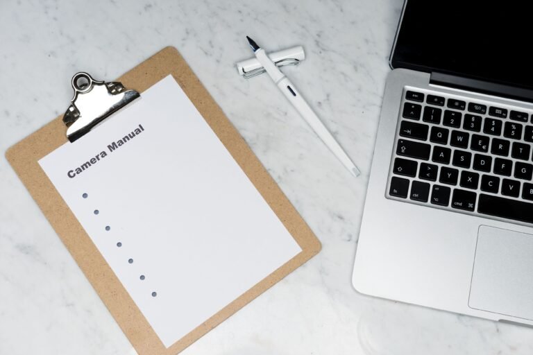 Clipboard, pen, and laptop arranged on a light marble desk.