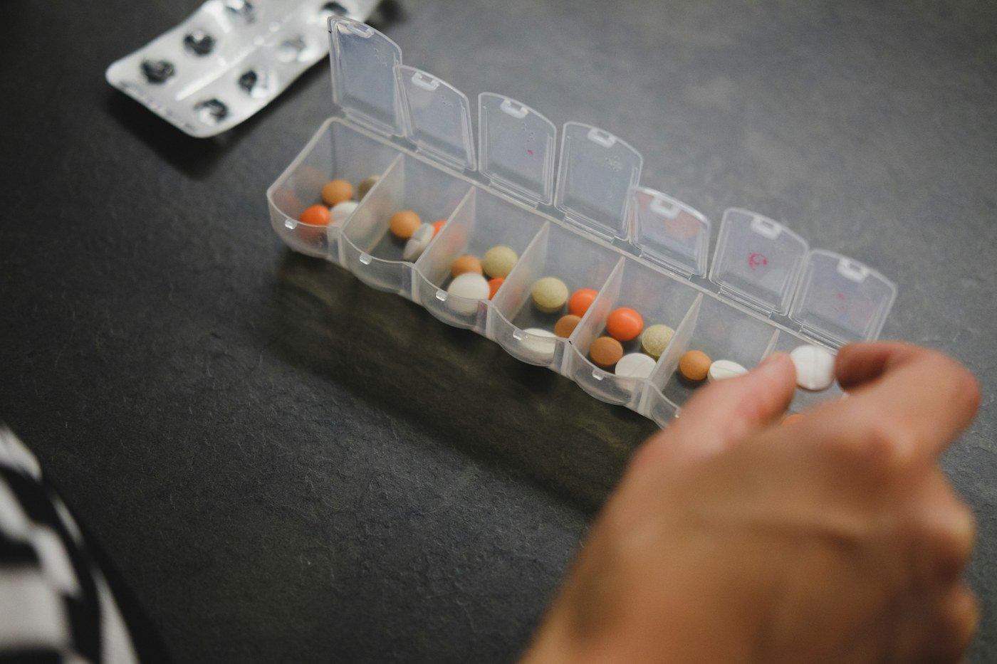 Hand reaching toward a weekly medication organizer with labeled compartments