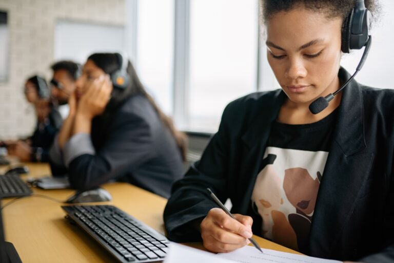 Call-center worker wearing a headset and taking notes at a desk.