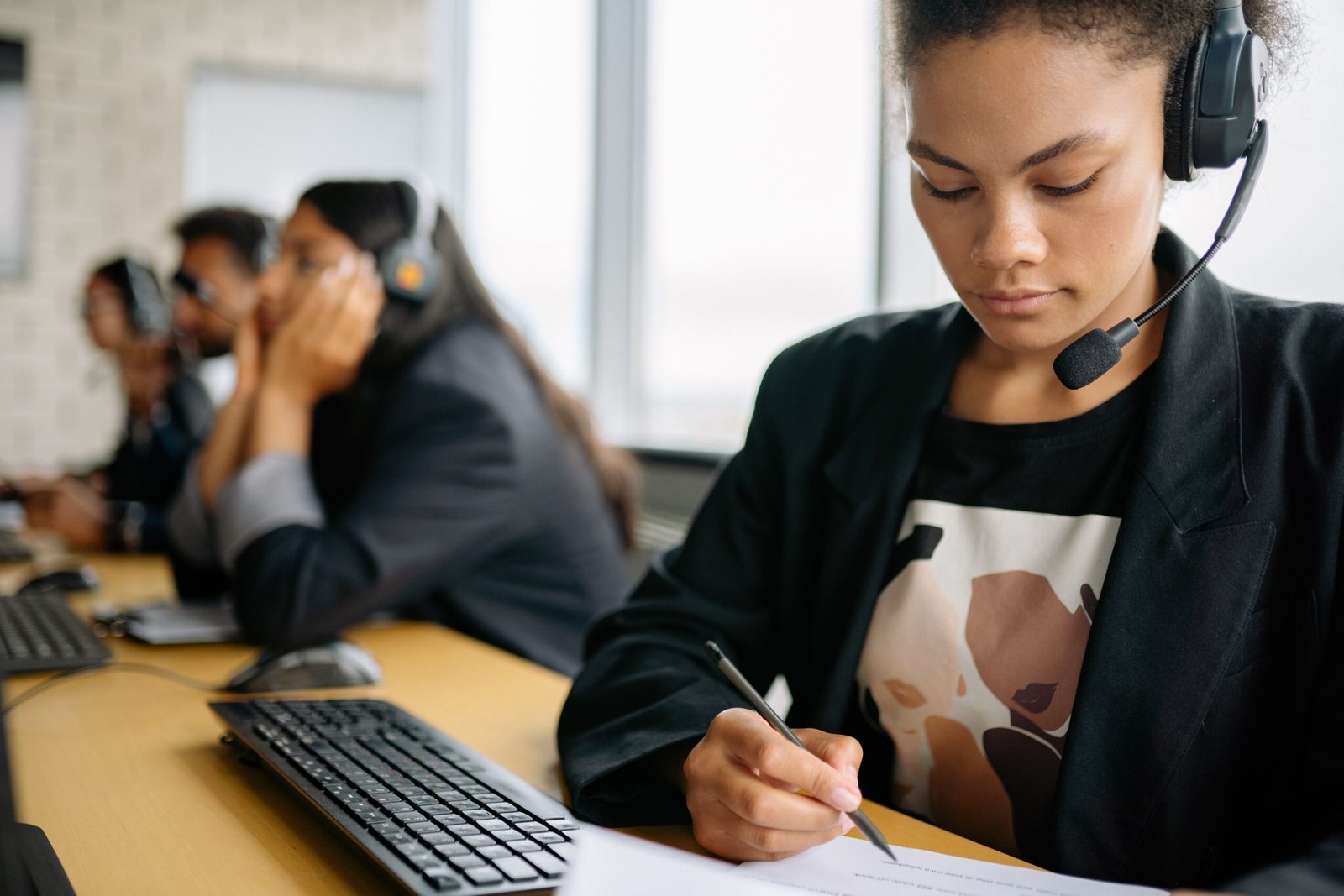 Call-center worker wearing a headset and taking notes at a desk.