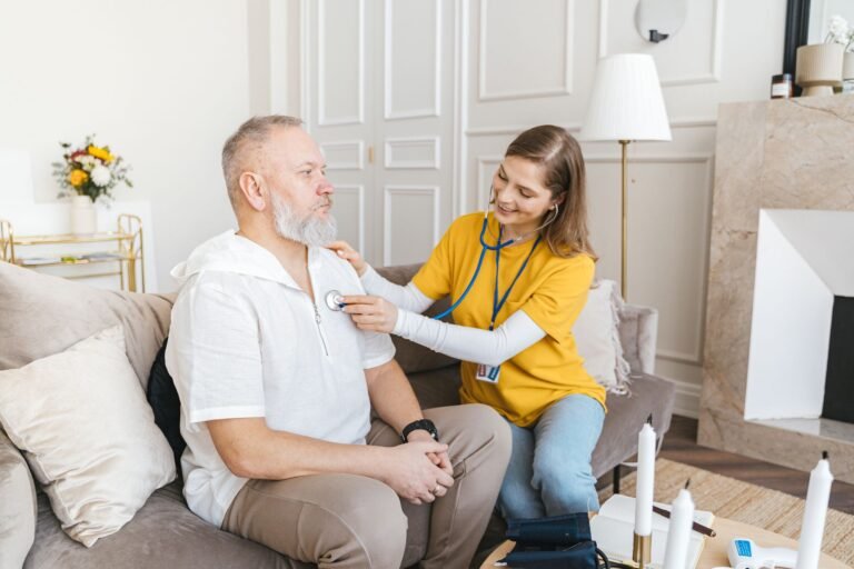 Healthcare professional using a stethoscope during a home visit with an older adult.