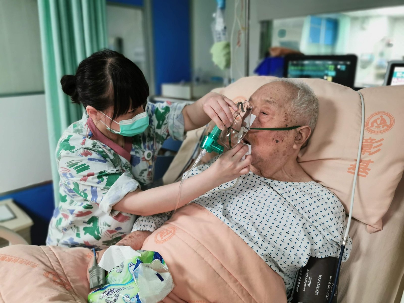 Nurse caring for an older patient using oxygen in a hospital bed