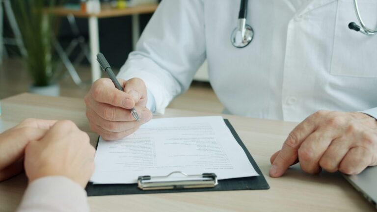 Clinician reviewing a medical form on a clipboard with a patient seated across the desk