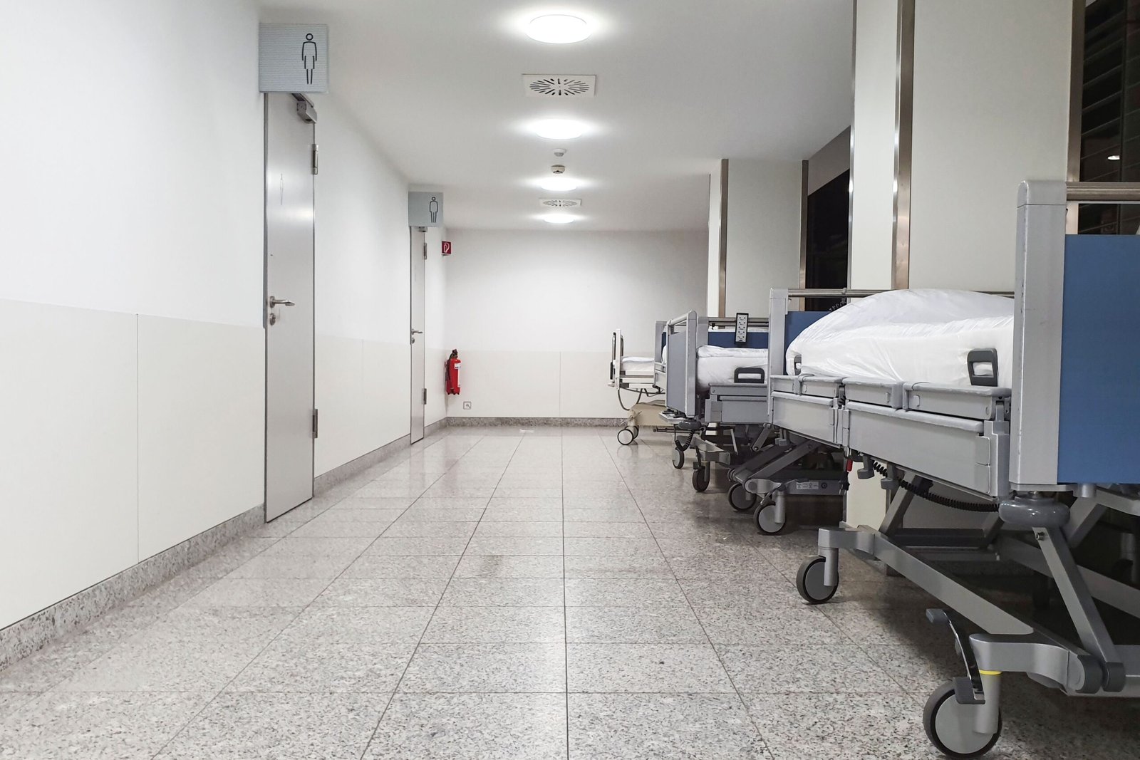Empty medical beds positioned in a modern hospital hallway.