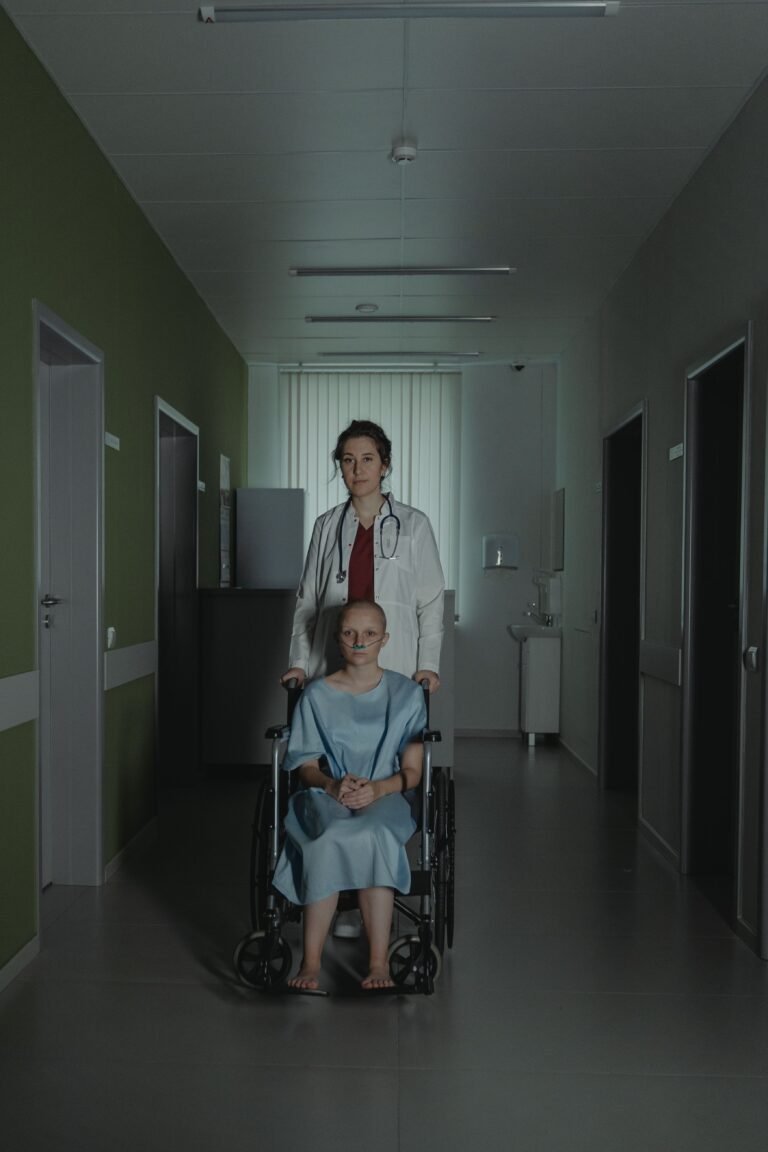 Healthcare professional assisting a wheelchair user in a hospital corridor.