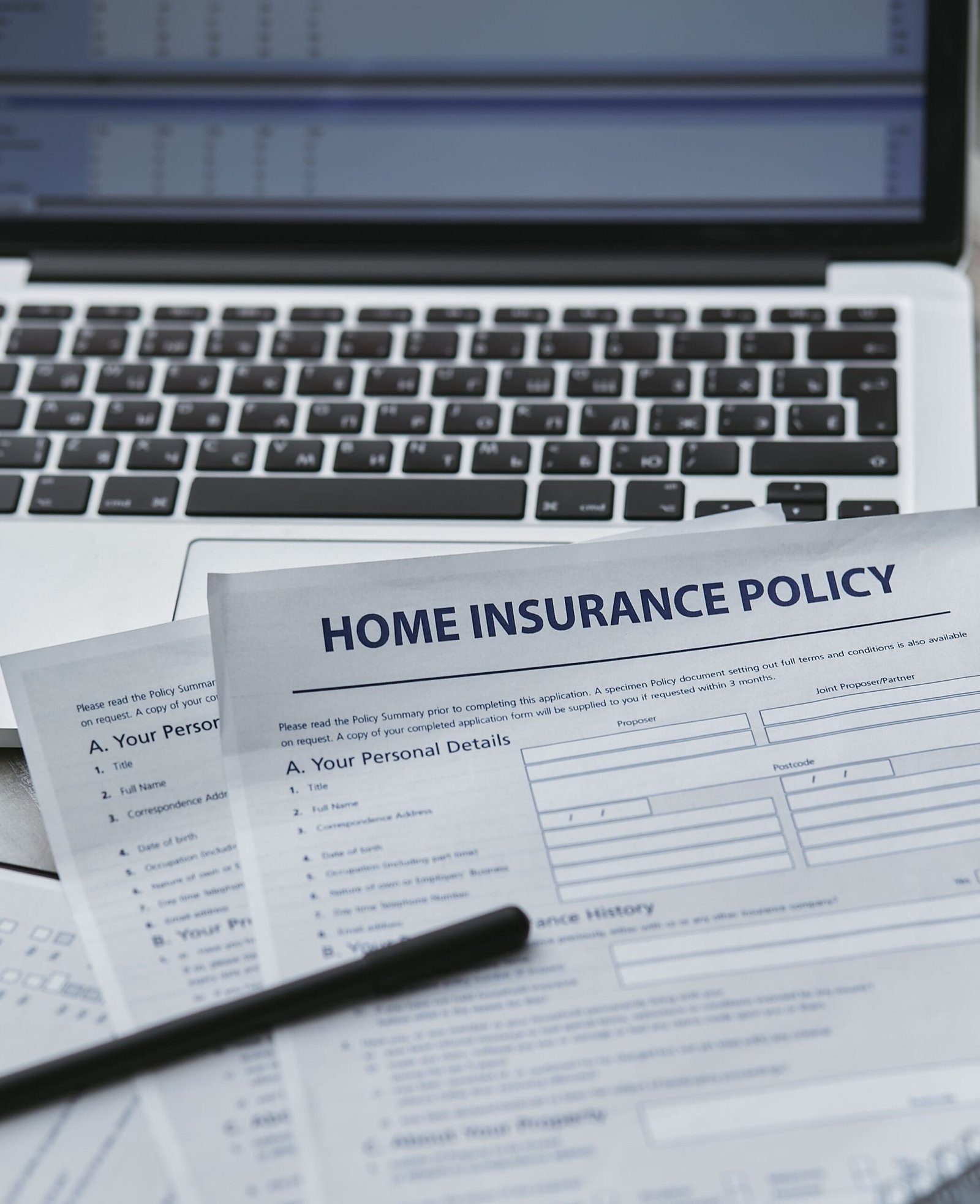 Insurance policy paperwork beside a laptop on a desk.