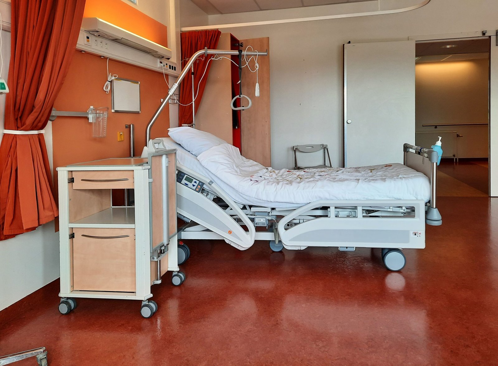 Empty adjustable healthcare bed with bedside equipment in a clean room.