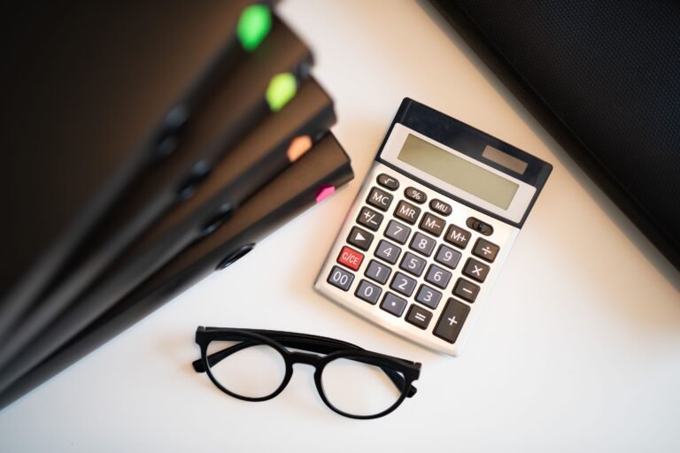 Calculator, glasses, and financial folders arranged on a desk.