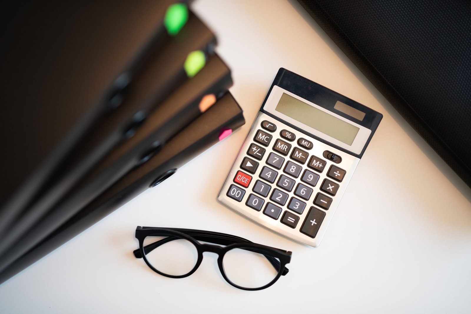 Calculator, glasses, and financial folders arranged on a desk.