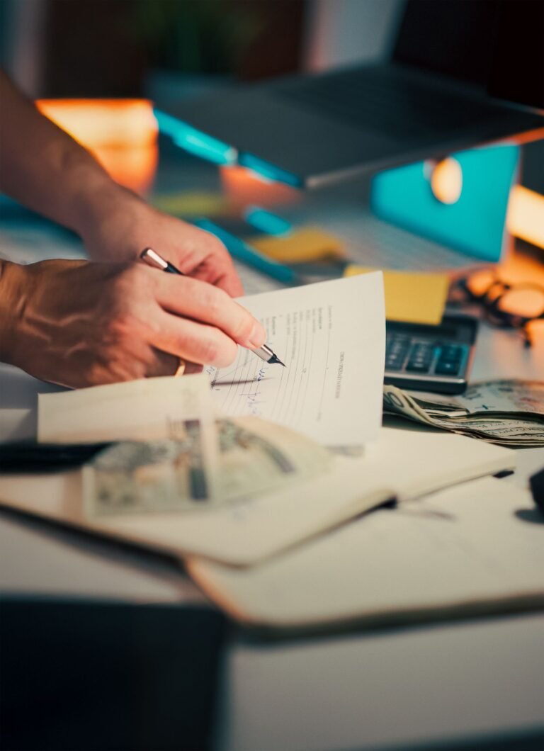 Hand signing financial documents beside cash and a calculator.