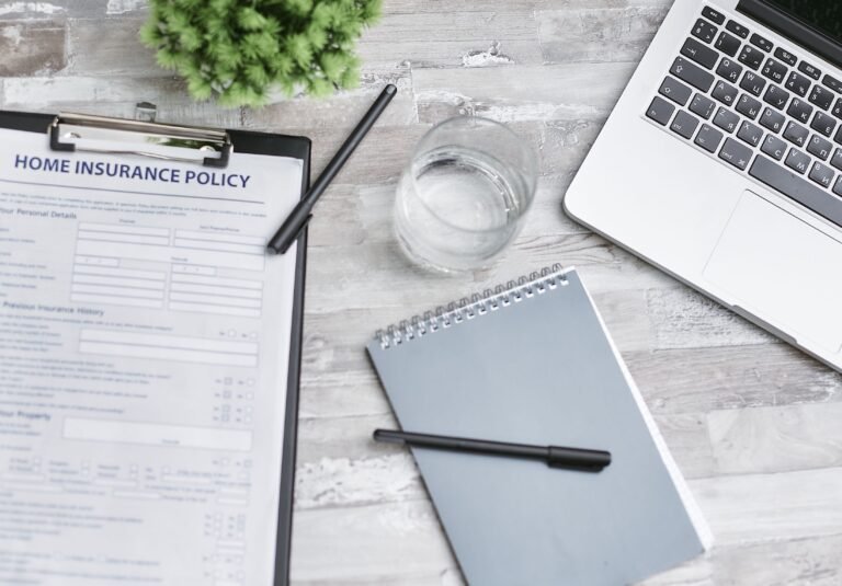 Notebook, laptop, and insurance documents arranged on a desk.