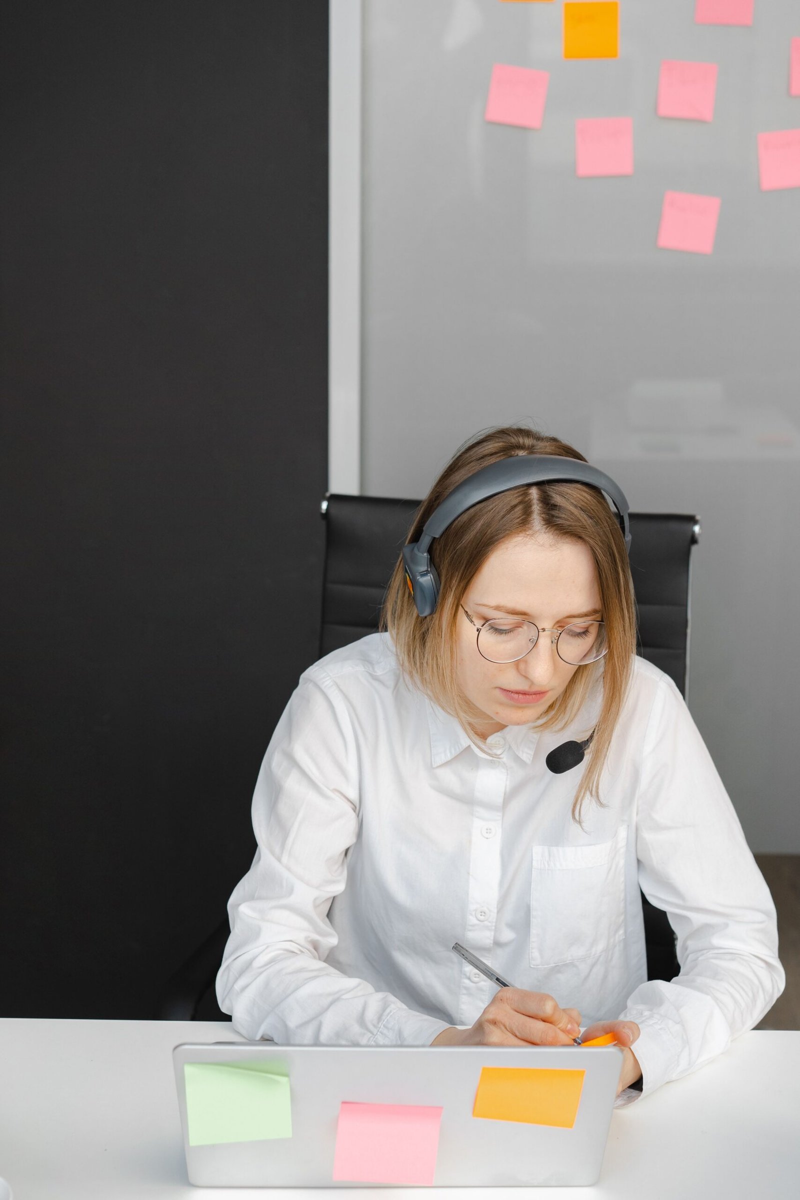 Customer-service worker wearing a headset and writing notes at a desk.