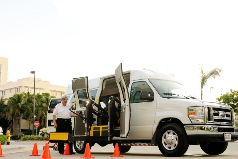 Wheelchair-accessible transport van with open doors and ramp outdoors.
