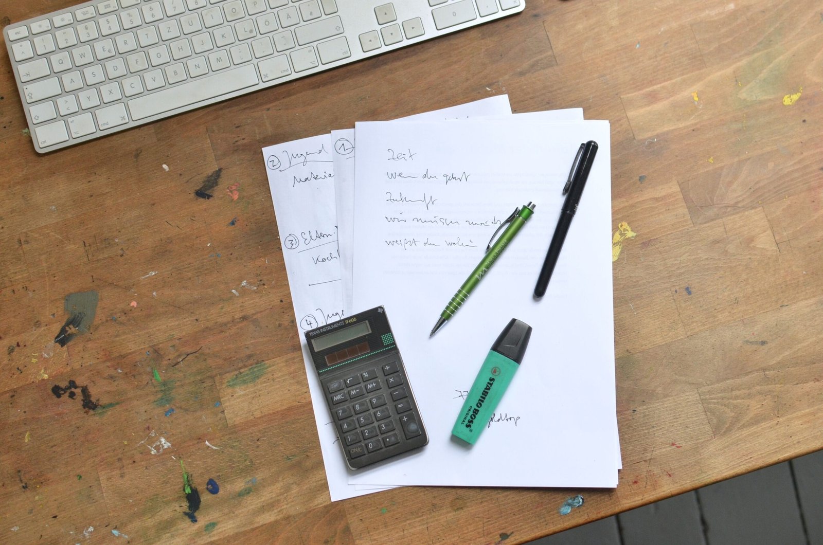 Paperwork, calculator, keyboard, and pens arranged on a desk.