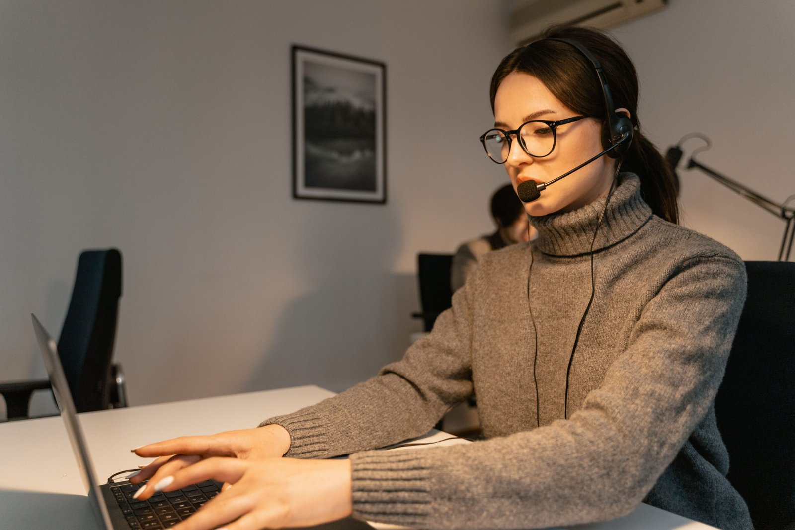 Customer-support professional using a headset and laptop at a desk.