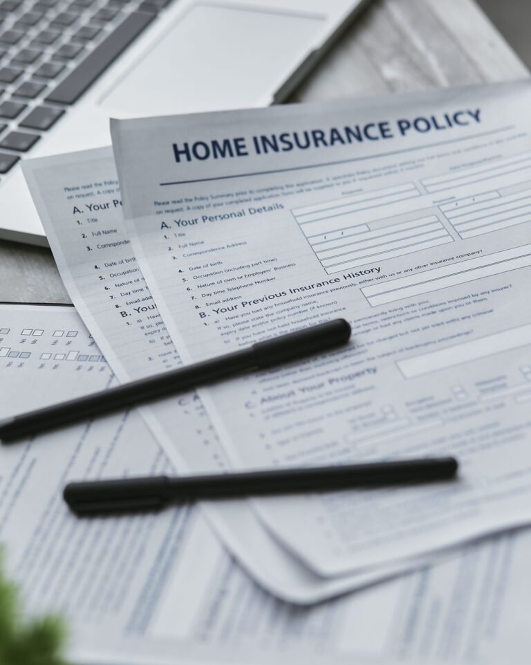 Insurance documents and writing tools arranged beside a laptop.
