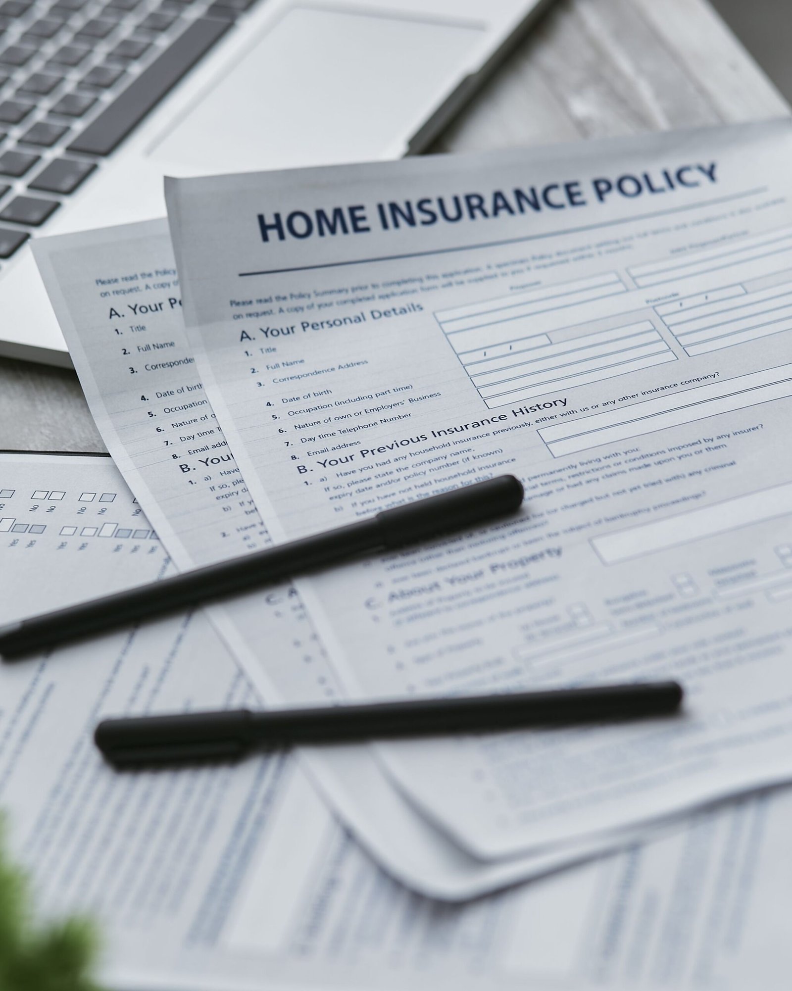 Insurance documents and writing tools arranged beside a laptop.