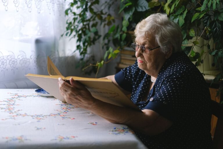 Older woman reading at a table in a quiet home setting.