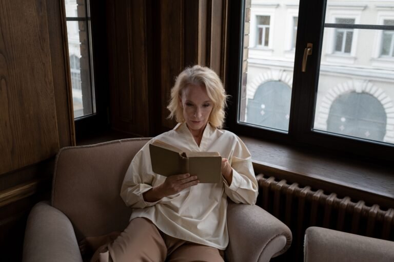 Older woman reading by a window in a calm room.