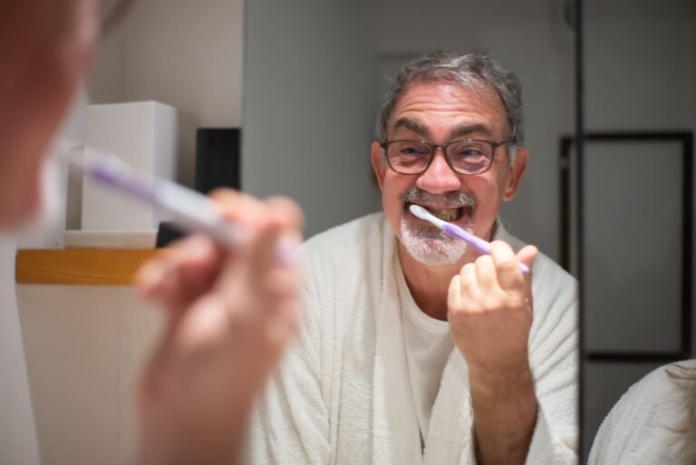 Older man brushing his teeth in front of a bathroom mirror