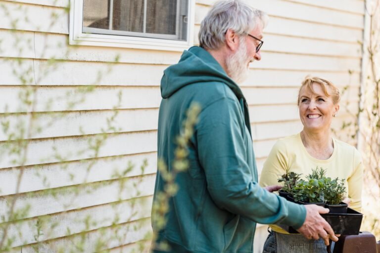 Older couple smiling and talking while holding a tray of small potted plants outdoors