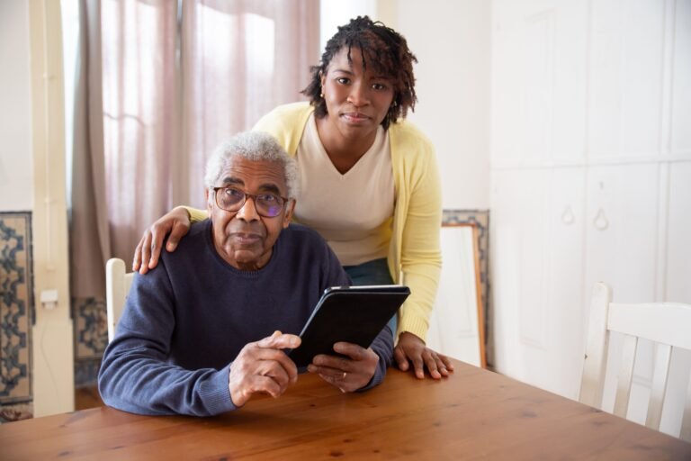 Older man and caregiver looking at a tablet together at home.