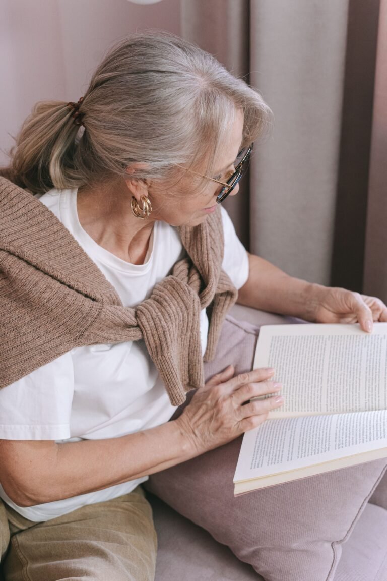 Older woman reading a book in a comfortable home setting.