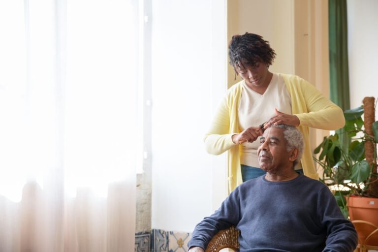 Caregiver helping an older man with grooming near a window
