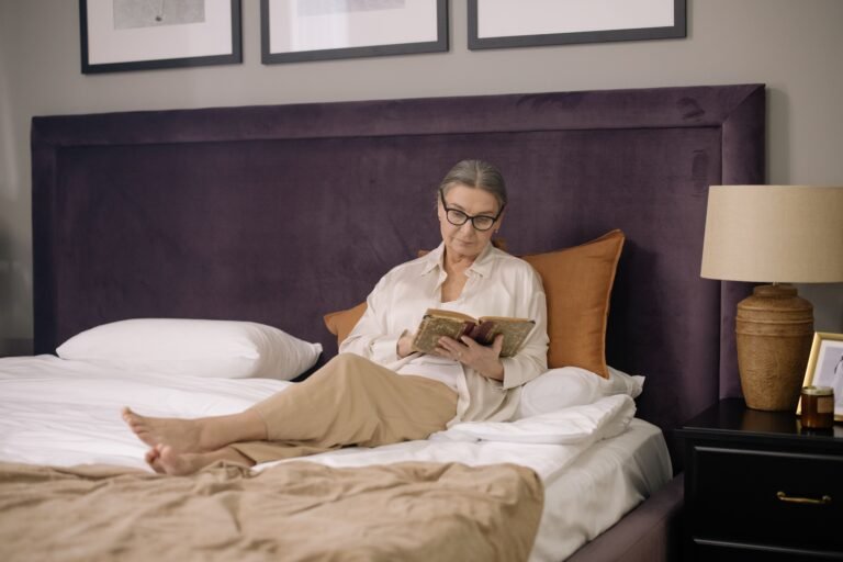 Older woman seated on a bed in a comfortable bedroom