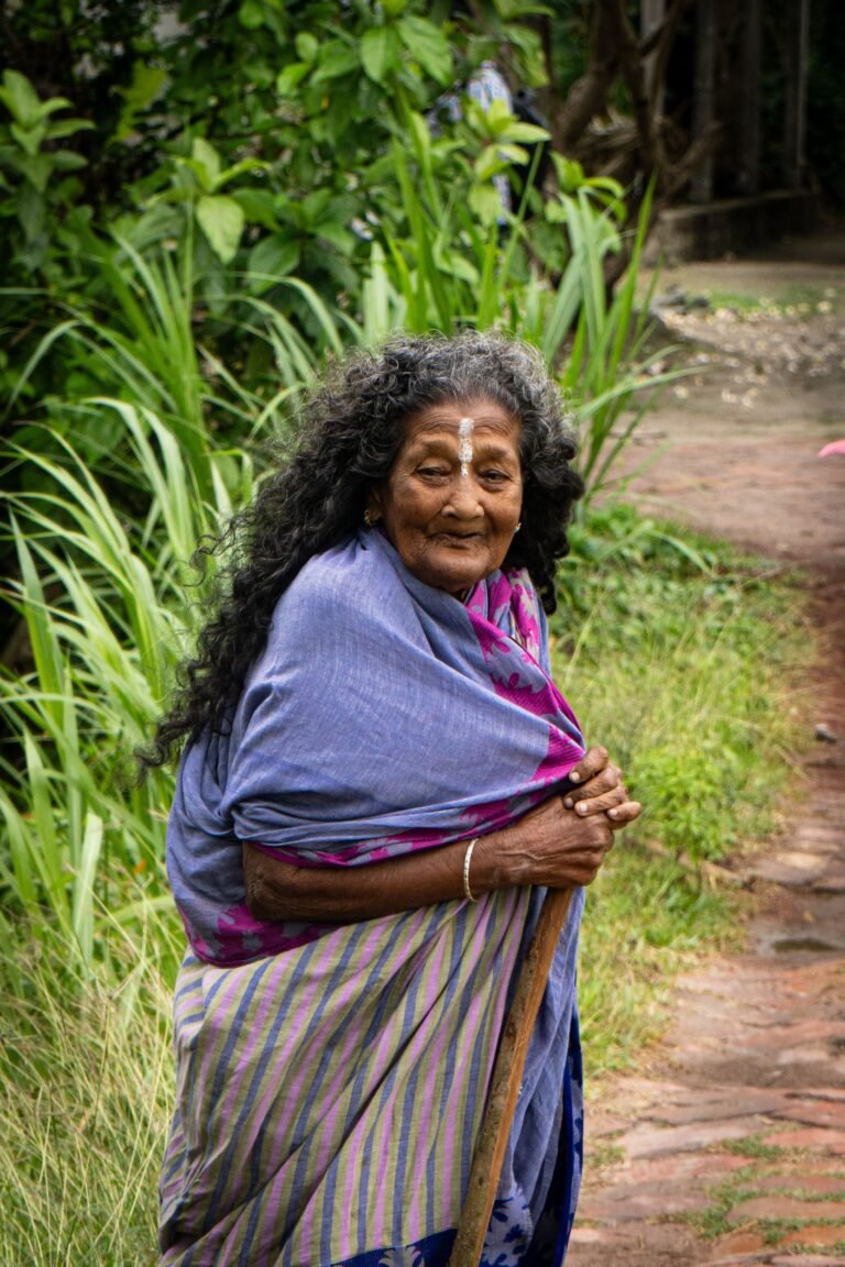Older woman walking along a garden path with a cane.