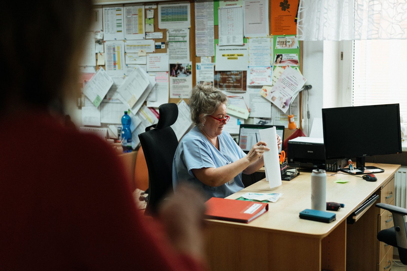 Healthcare worker in blue scrubs organizing paperwork at an office desk.