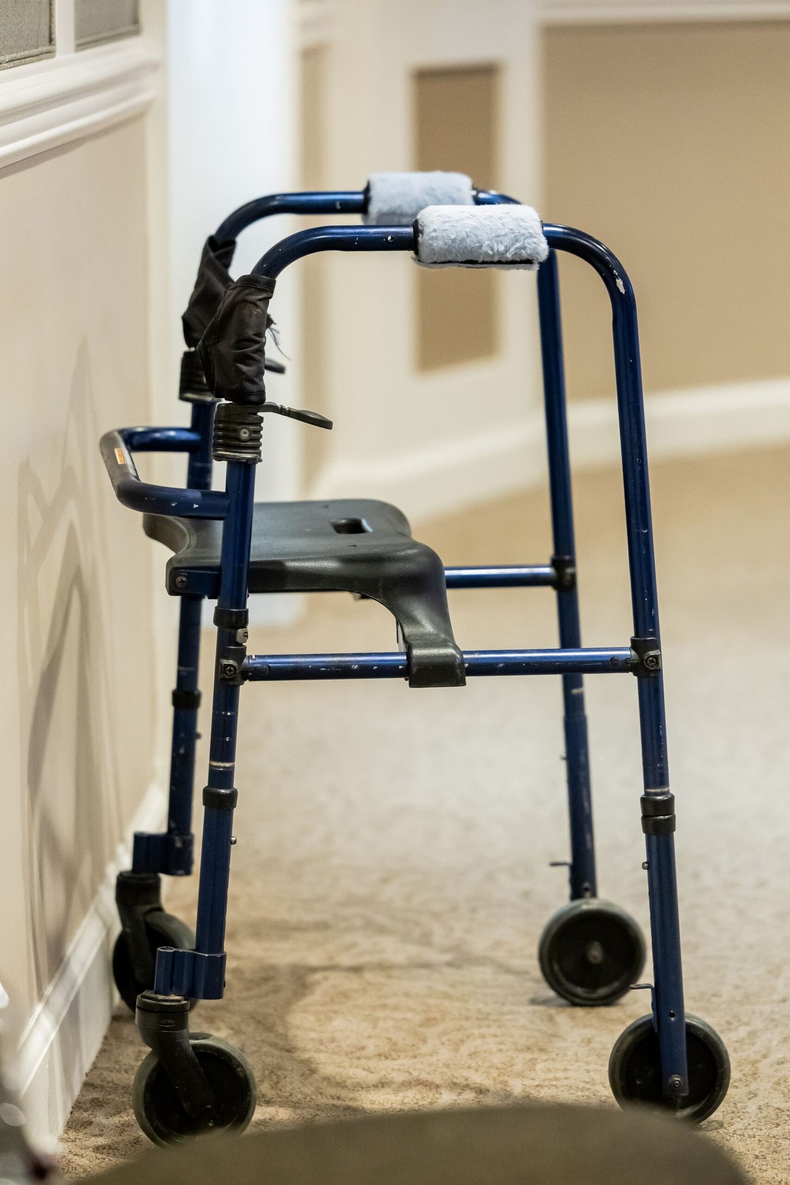 Blue rolling walker standing beside a wall in a carpeted hallway.