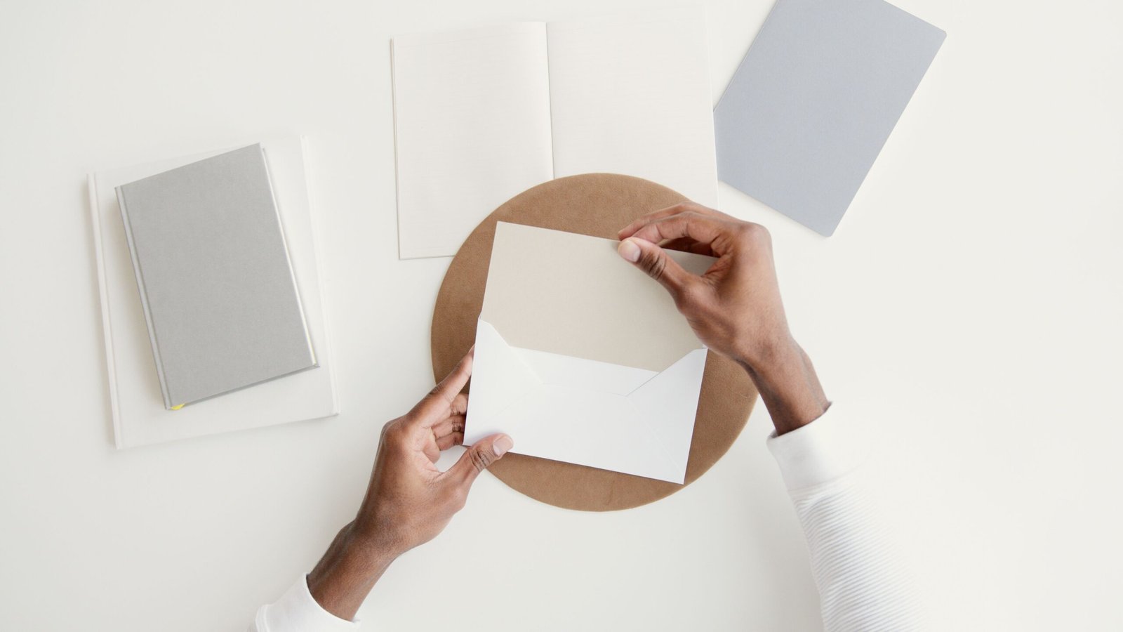 Hands opening an envelope beside notebooks on a clean desk.