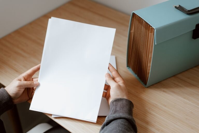 Hands holding blank papers beside a turquoise document file box.