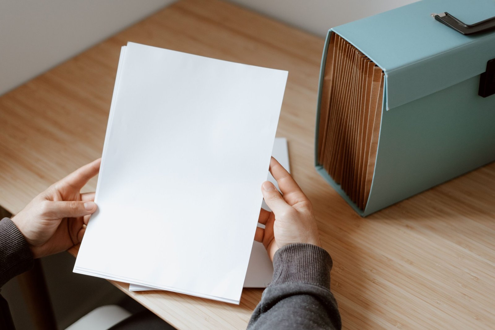 Hands holding blank papers beside a turquoise document file box.