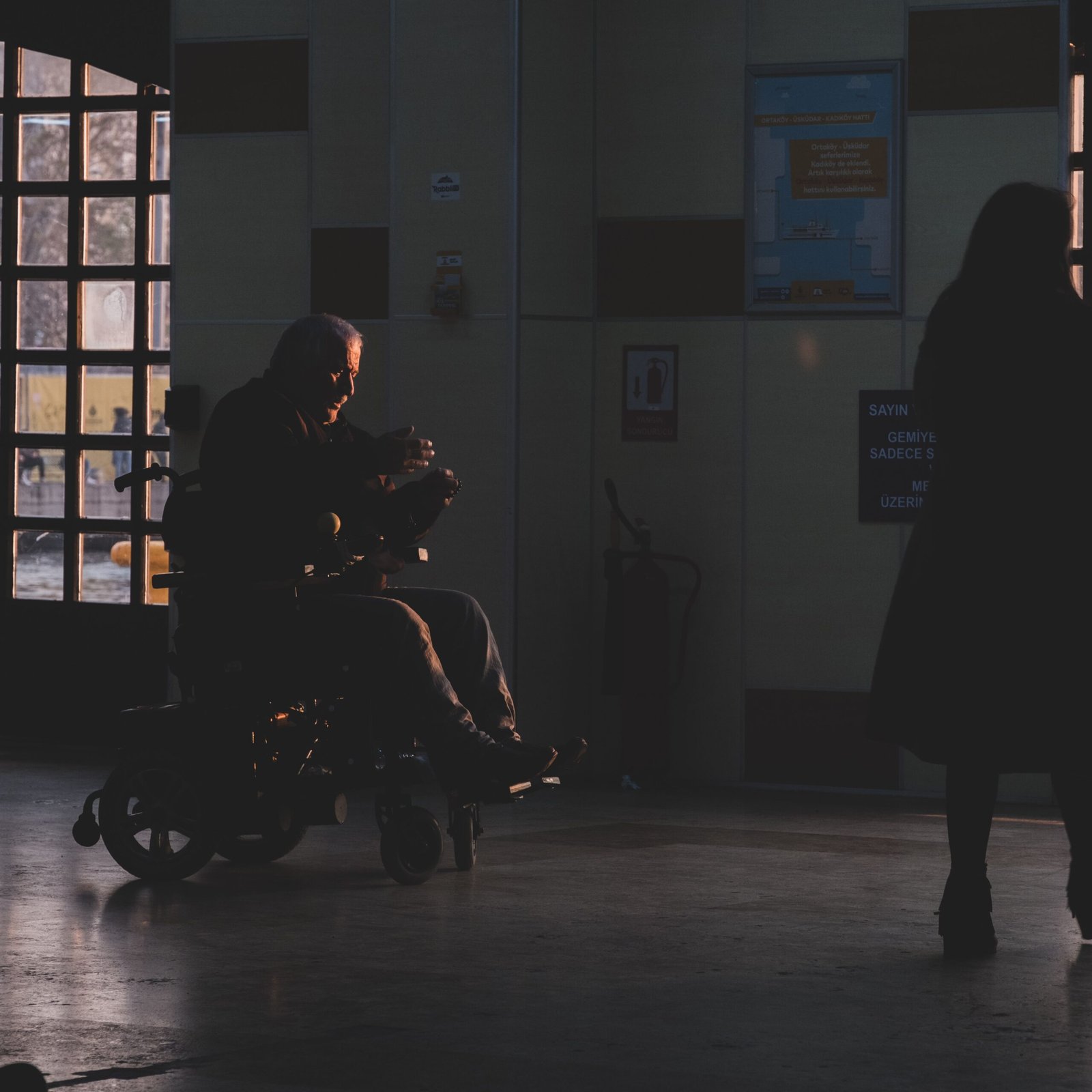 Wheelchair user silhouetted in a healthcare corridor.