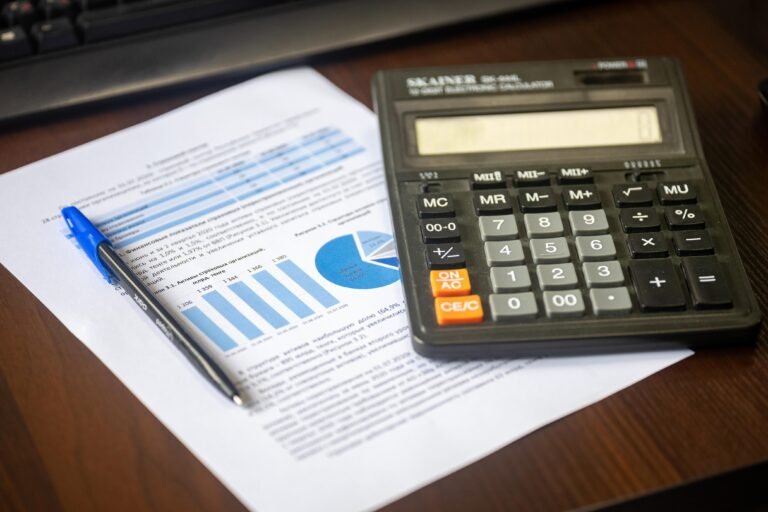 Calculator, pen, and financial report arranged on a wooden desk.