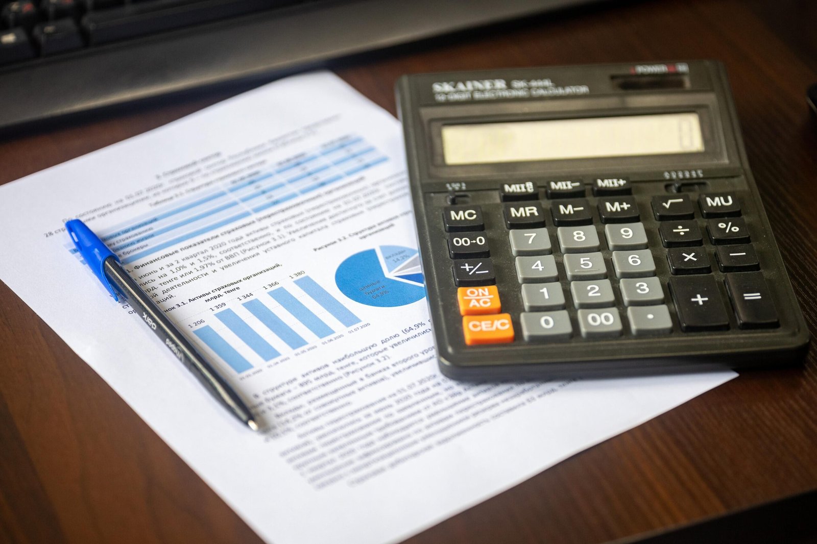Calculator, pen, and financial report arranged on a wooden desk.