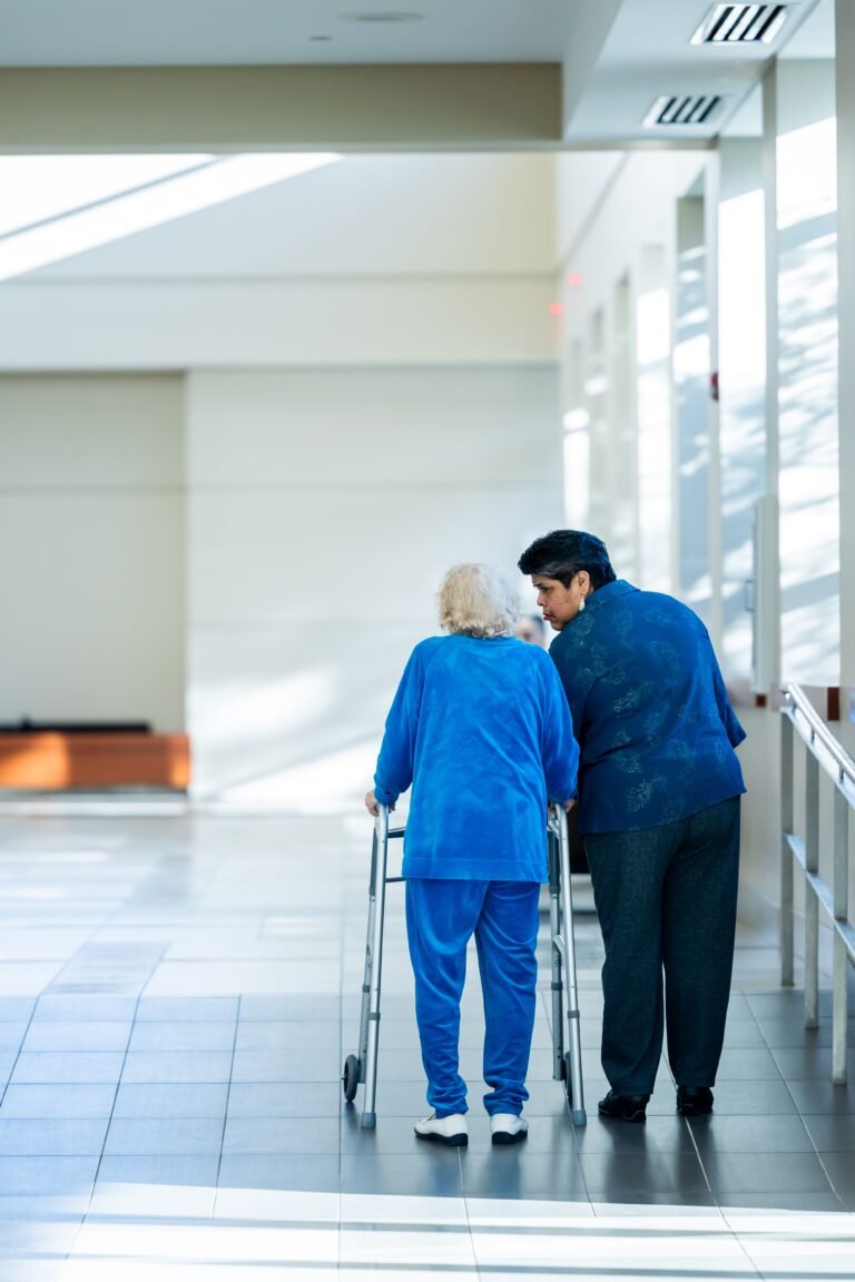 Nurse assisting an older woman using a walker in a healthcare corridor